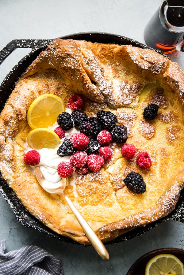 Dutch baby pancake in a cast iron skillet with fresh berries, butter, lemon and maple syrup