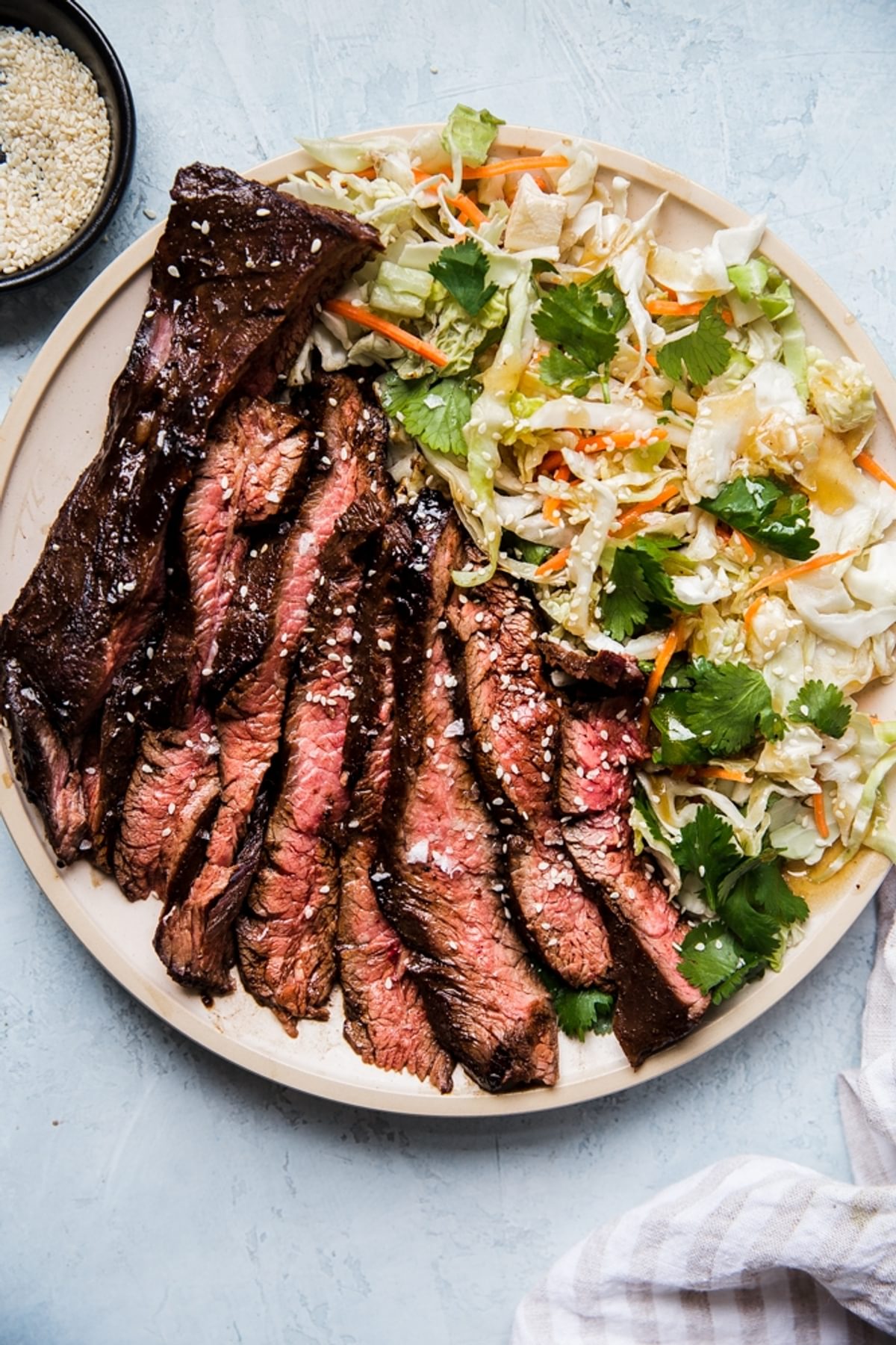 thin slices of grilled flank steak marinated in hoisin and five spice next to an asian salad on a plate