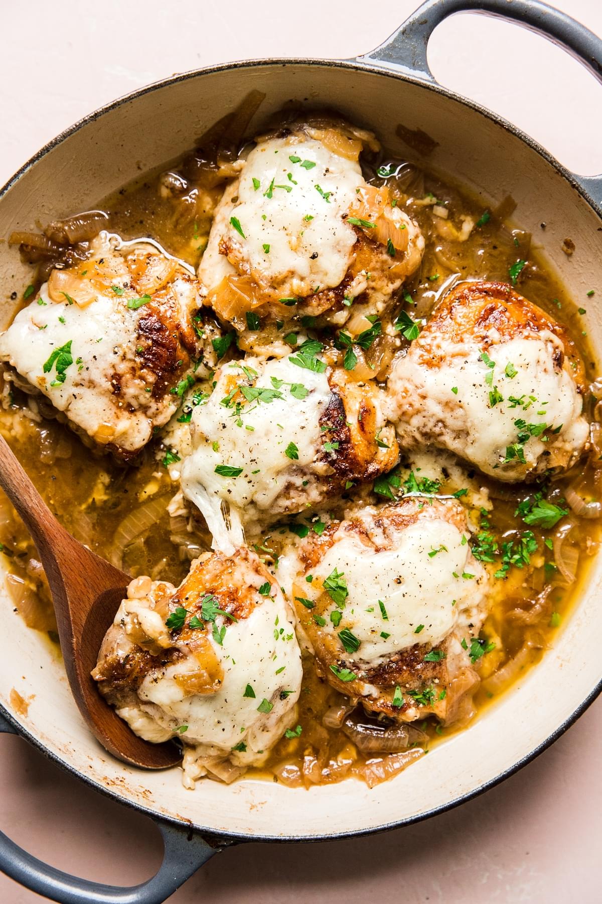 french onion chicken with gruyere cheese being scooped out of a pan with a wooden spoon