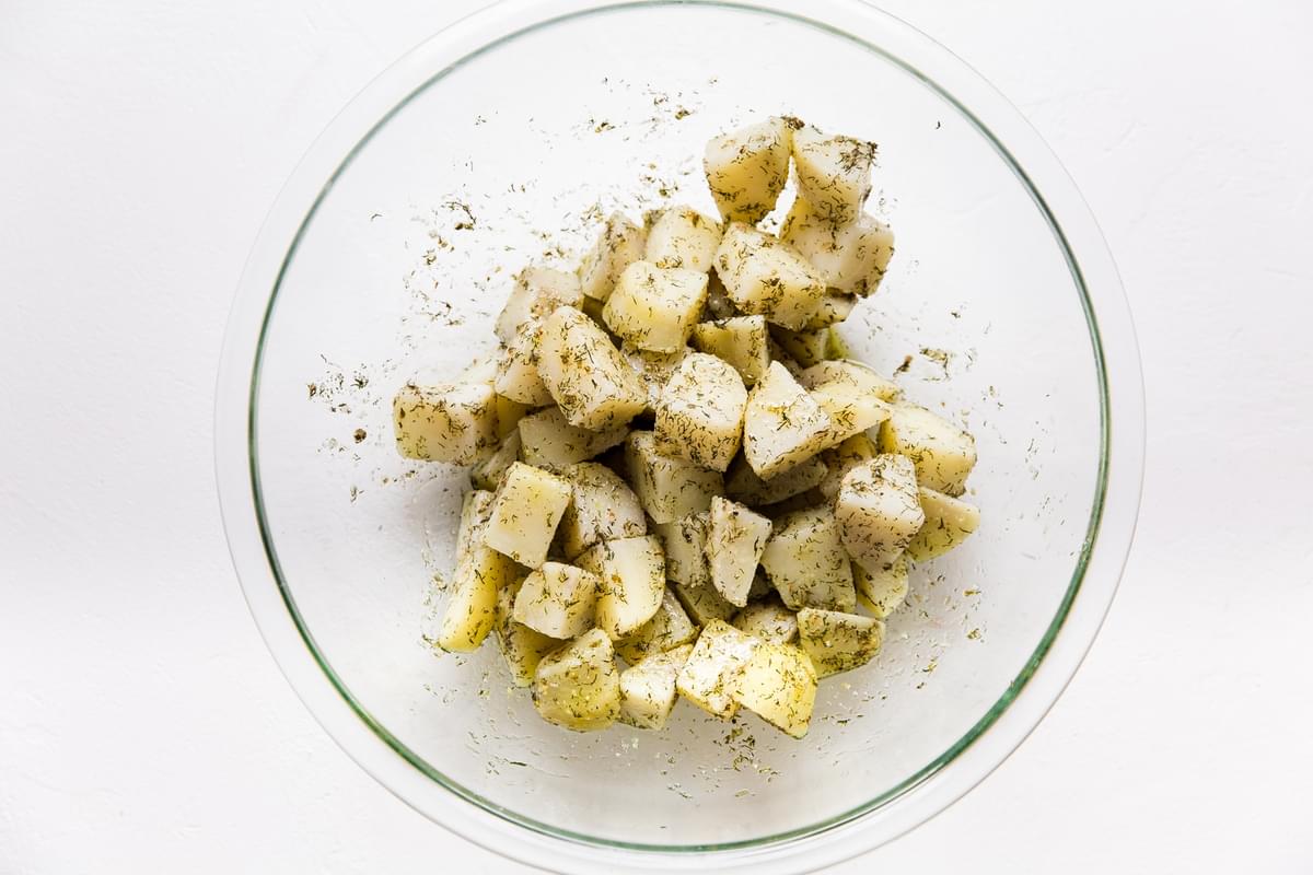 cut par boiled potatoes in a bowl marinated with olive oil dill, oregano and garlic