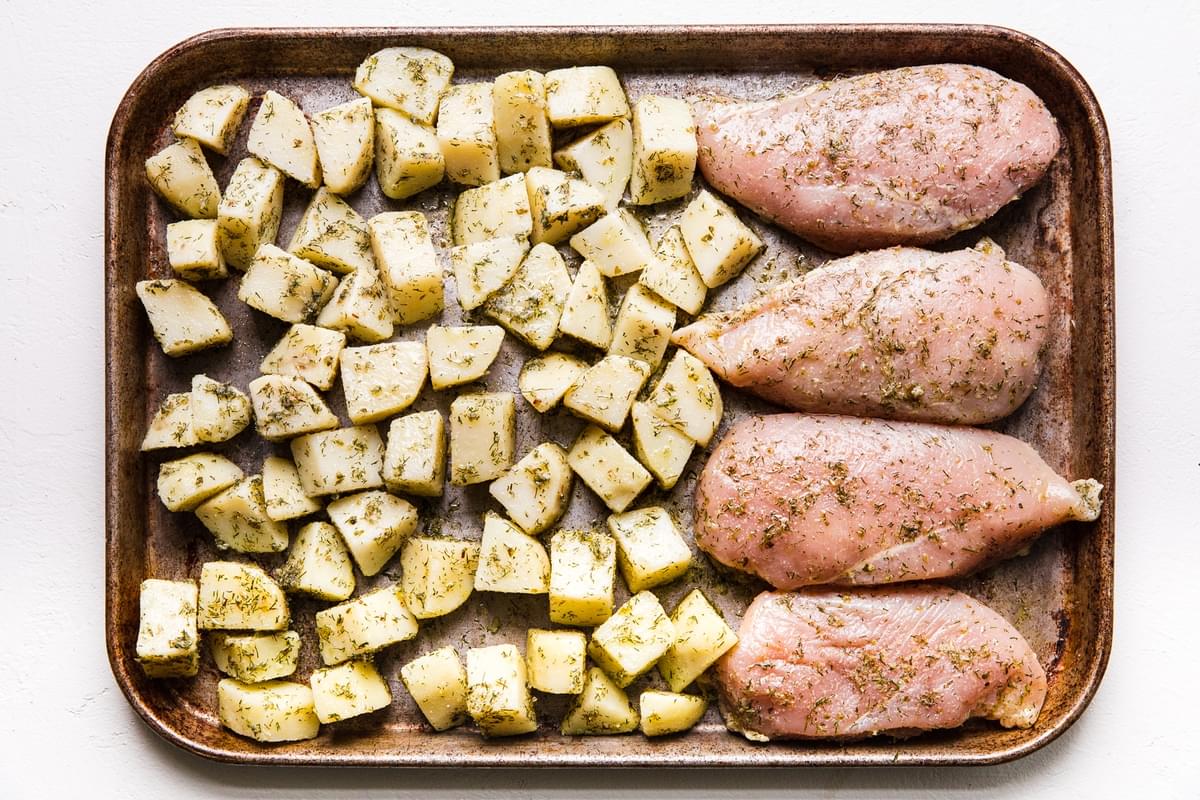 Greek Chicken sheet pan dinner about to go into the oven, potatoes and chicken breasts in a Greek marinade.