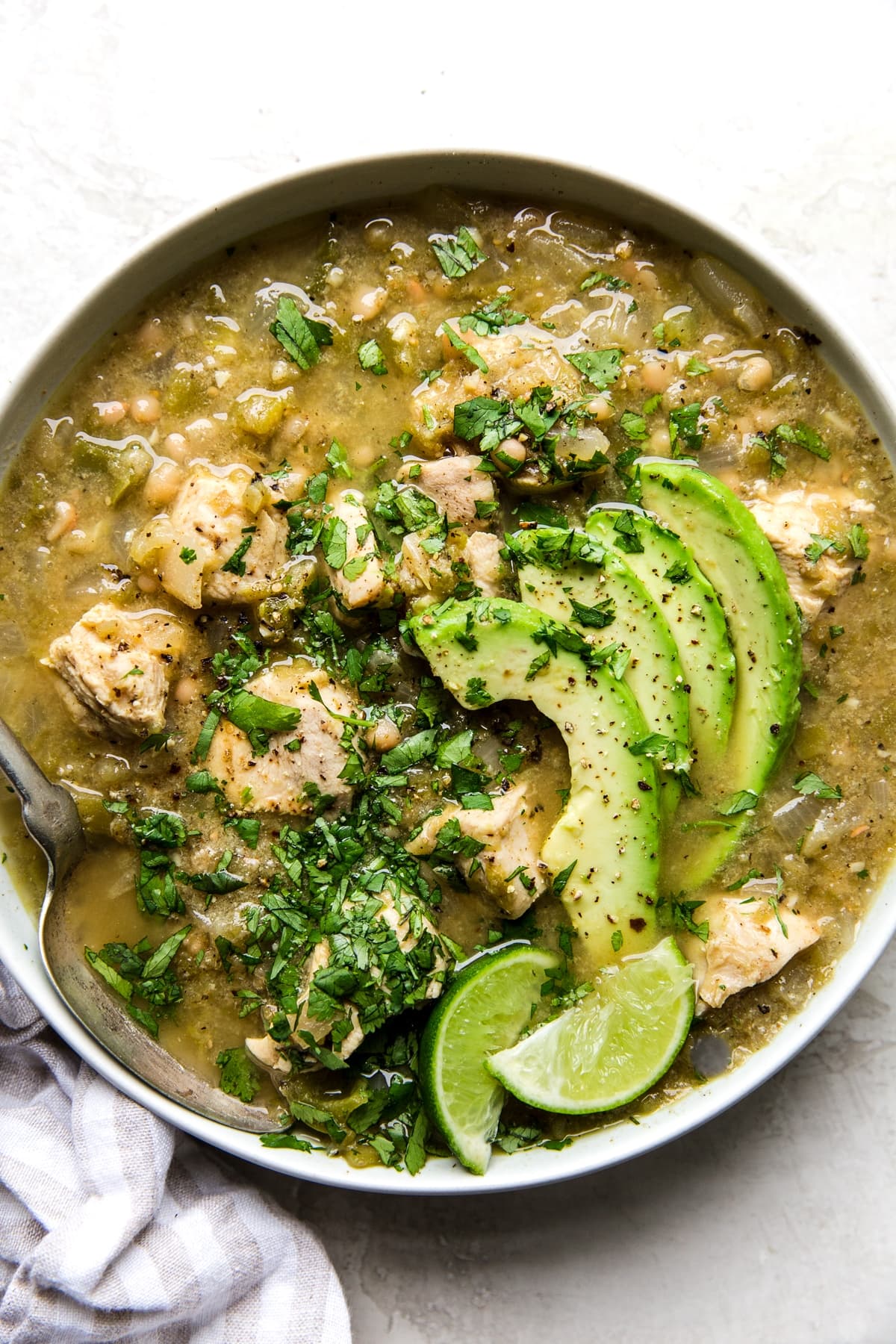 Green chicken chili verde soup in a bowl with avocado, lime and cilantro