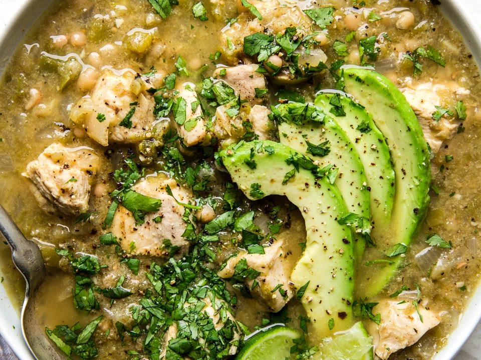 Green chicken chili verde soup in a bowl with avocado, lime and cilantro