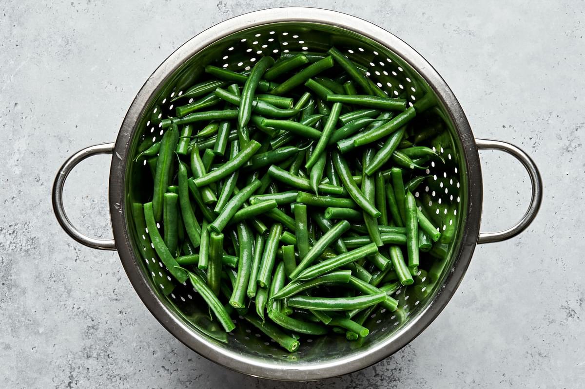 blanched green beans being drained in a colander