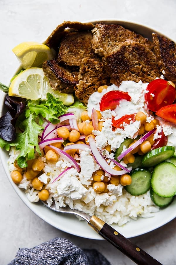 gyro bowl with cucumbers, lemon rice, feta, red onion, tomatoes, lettuce and gyro meat with a fork