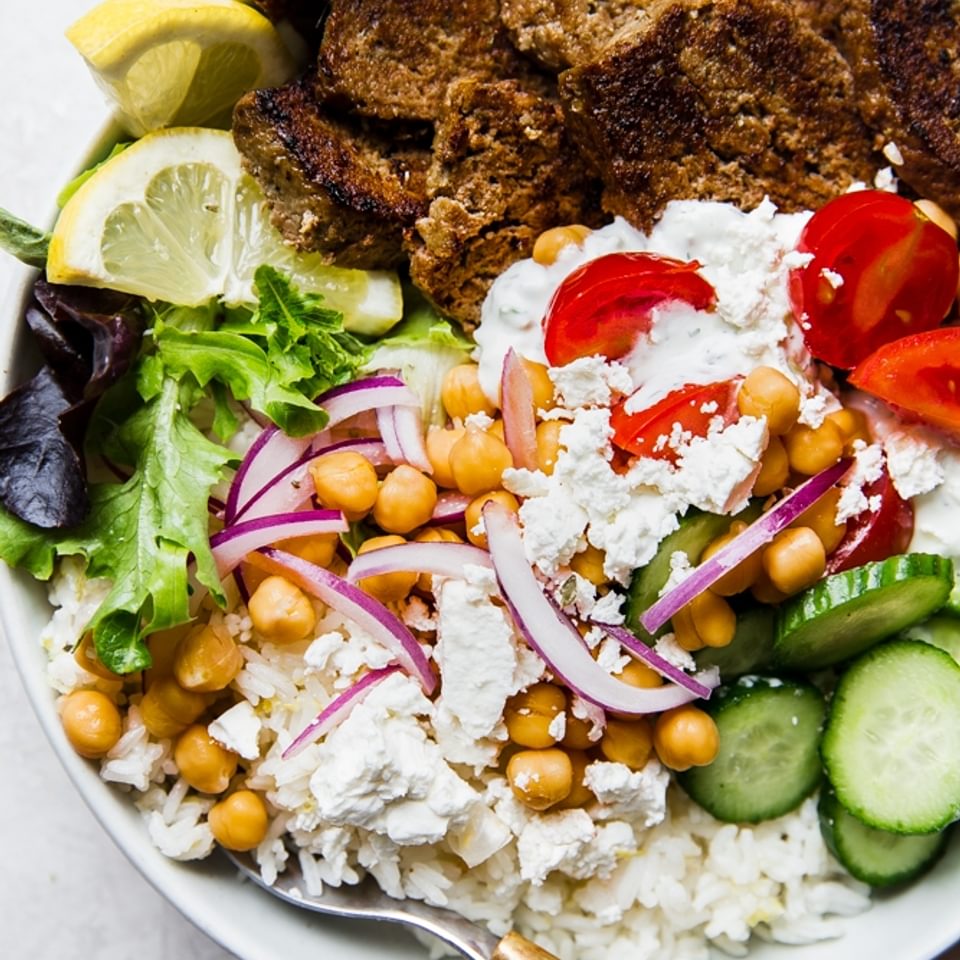 gyro bowl with cucumbers, lemon rice, feta, red onion, tomatoes, lettuce and gyro meat with a fork