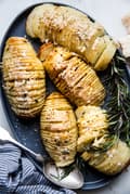 hasselback potatoes shown on a large platter with fresh herbs