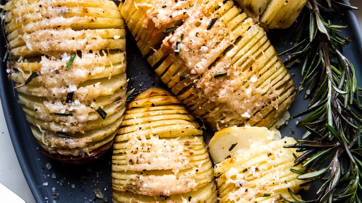 hasselback potatoes shown on a large platter with fresh herbs
