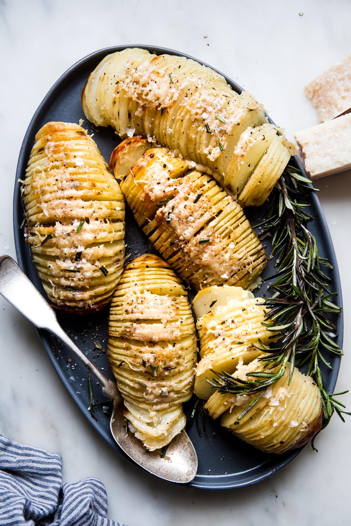 5 hasselback potatoes shown on a large oval platter with a spoon