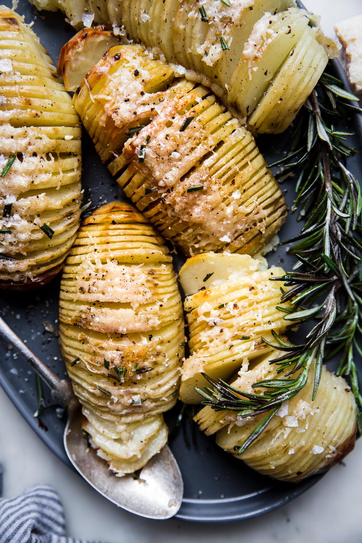 5 hasselback potatoes on a serving platter with fresh rosemary and parmesan