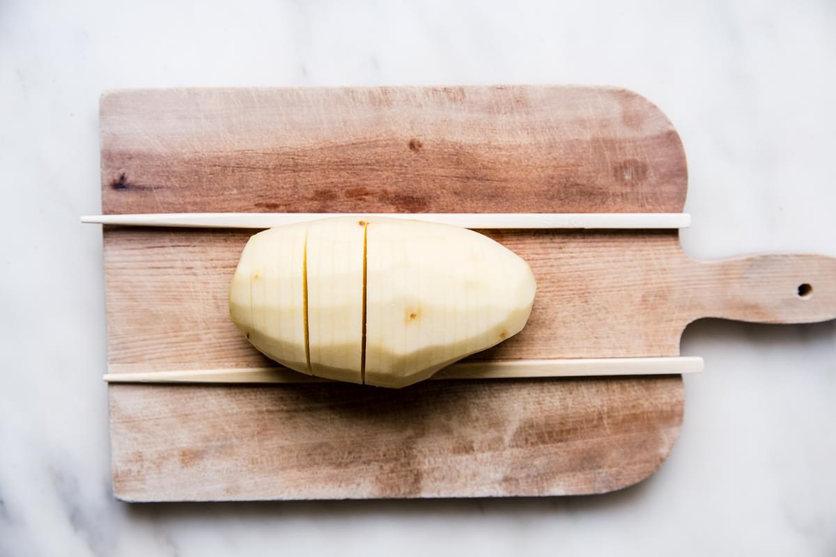 1 peeled russet potato on a cutting board with chop sticks next to it