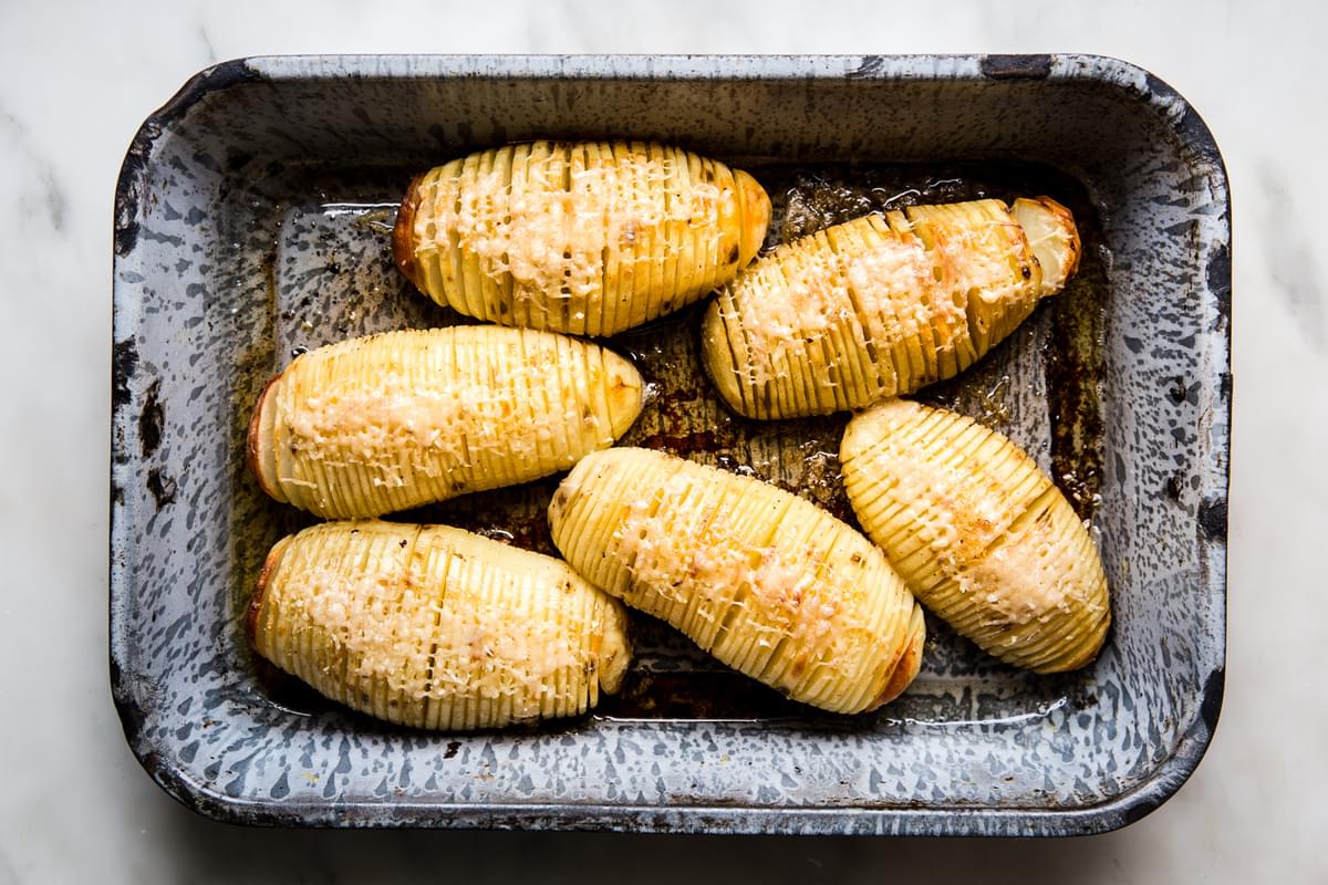 6 roasted hasselback potatoes in a baking dish topped with parmesan cheese and garlic butter