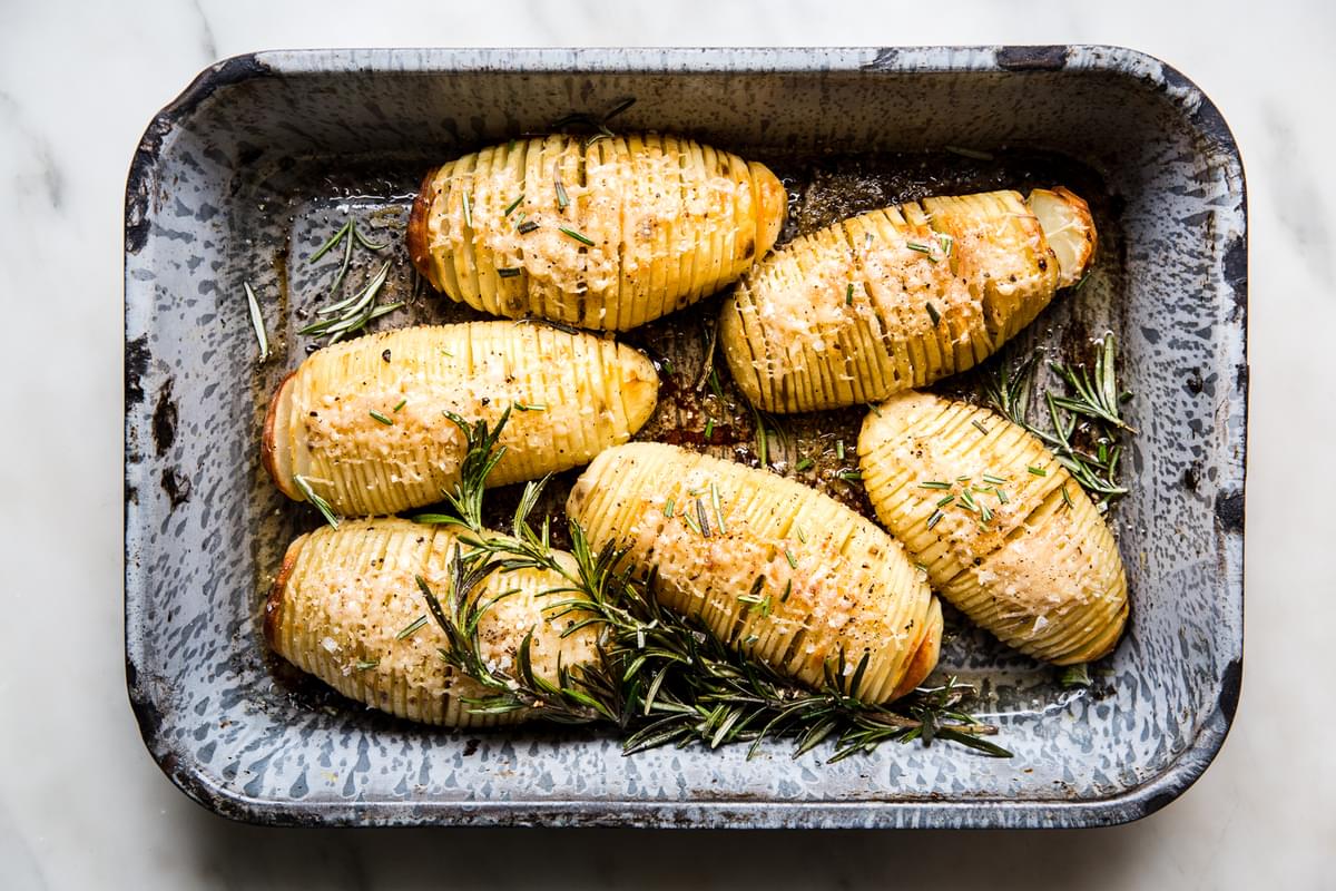 6 Hasselback potatoes in a baking dish with parmesan and rosemary.