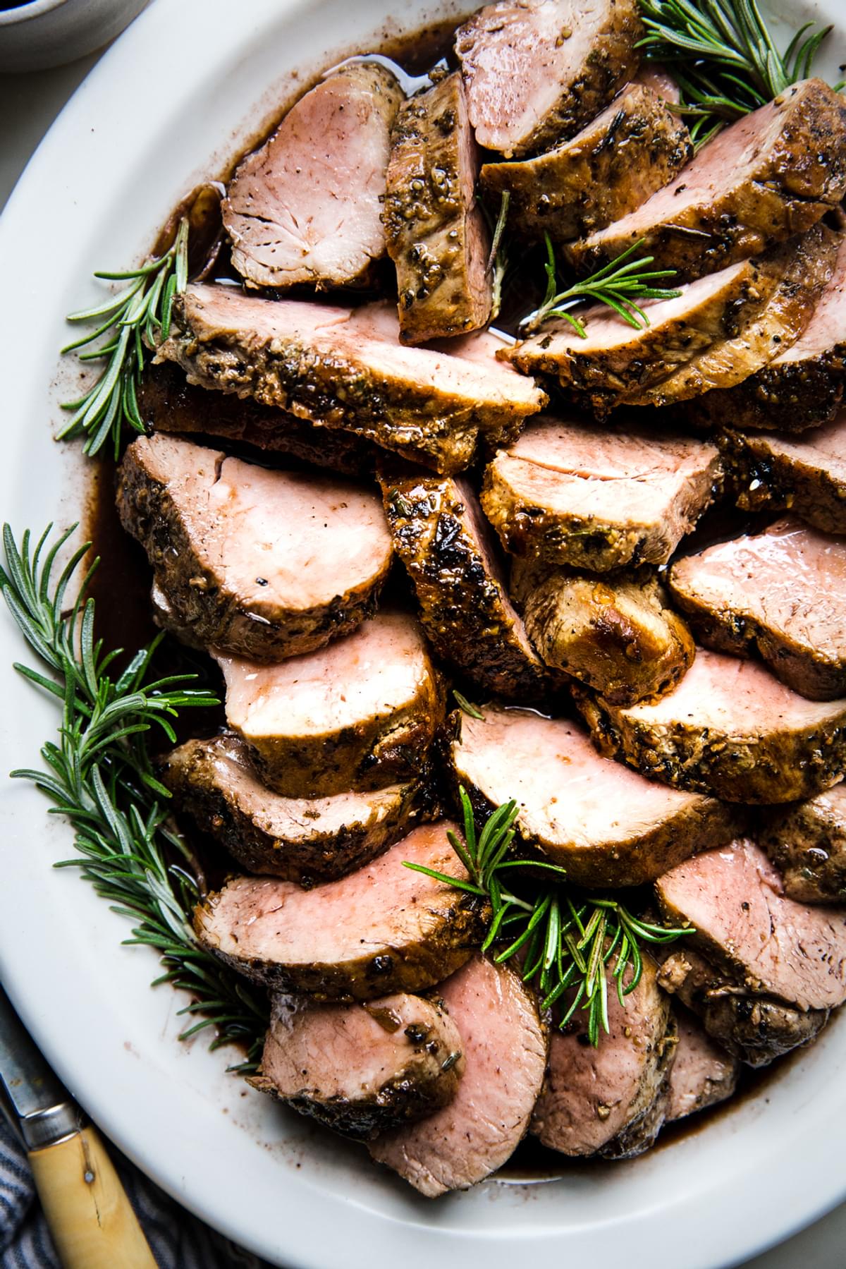 Herb crusted Pork Tenderloin with Port Wine Sauce on a white plate with rosemary