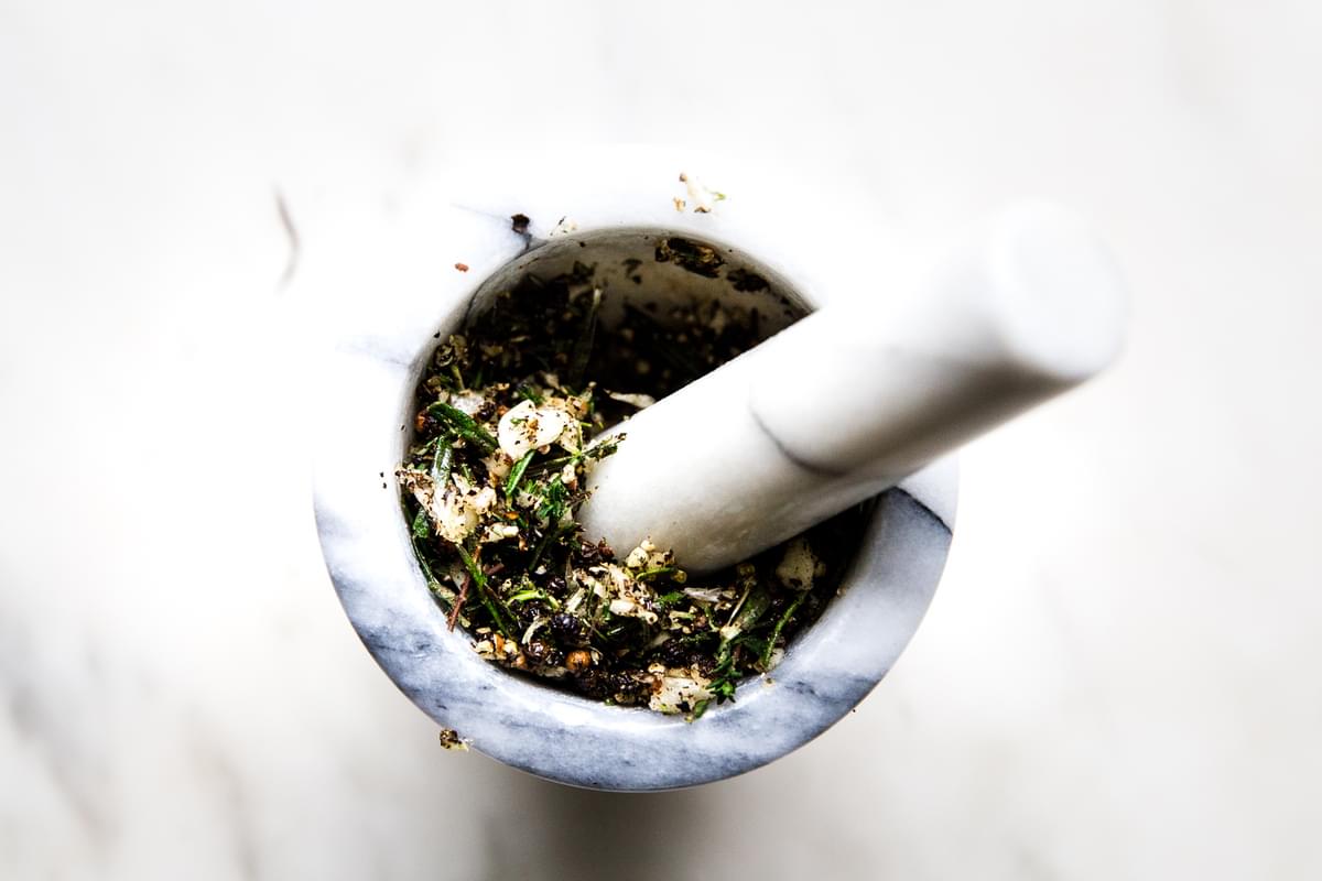 fresh rosemary and thyme in a mortar and pestle with garlic and peppercorns ground into a paste