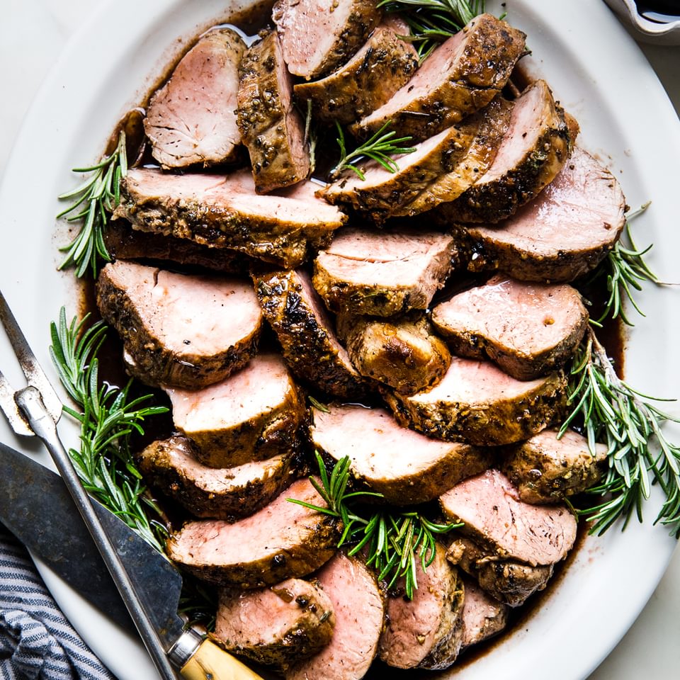 Herb crusted Pork Tenderloin with Port Wine Sauce on a white plate with rosemary