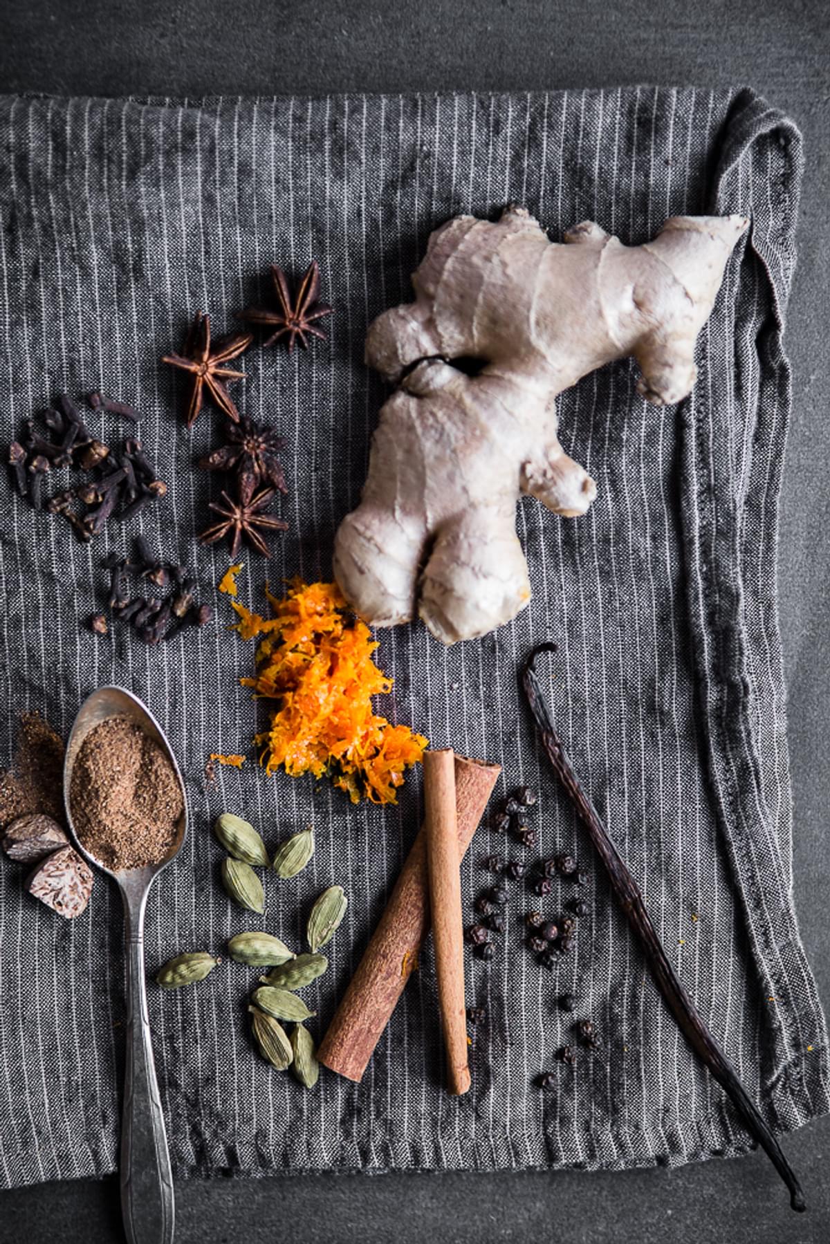 Ingredients for homemade Chai Tea concentrate laid out on a linen fresh ginger, anise, cloves, cinnamon, cardamom, vanilla