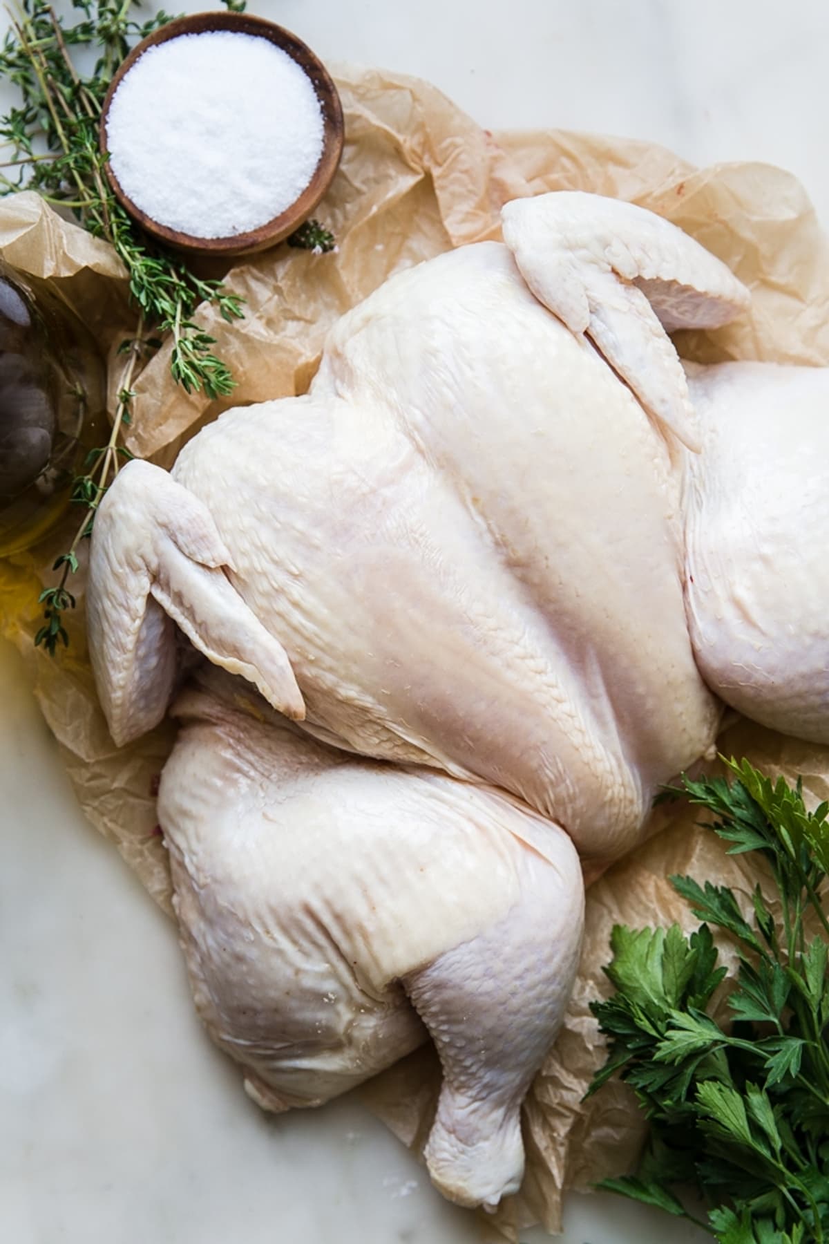 a spatchcocked chicken on parchment paper with salt thyme and parsley