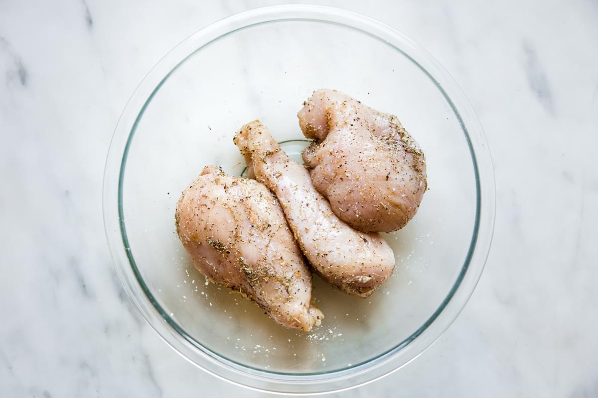 3 raw chicken breasts in a bowl with salt pepper and seasoning.
