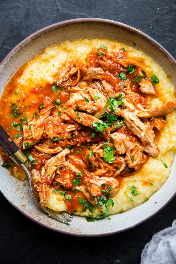 Shredded chicken thighs covered with marinara over polenta in a bowl with fresh basil