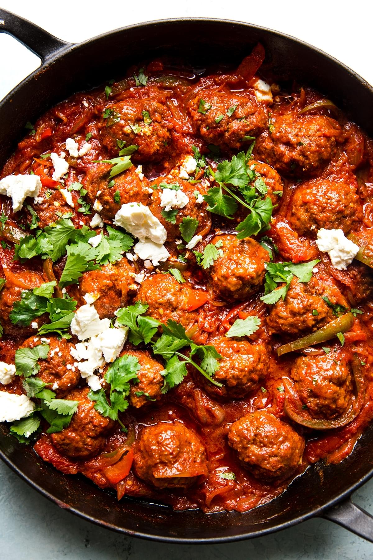 meatball shakshuka in a large skillet topped with fresh parsley and crumbled feta