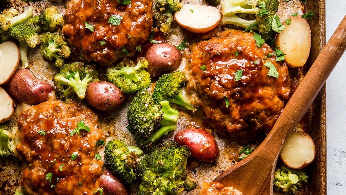 Mini Italian-StyleMeat loaf sheet pan with broccoli and roasted potatoes cut in half shown with a linen and a wooden spatula