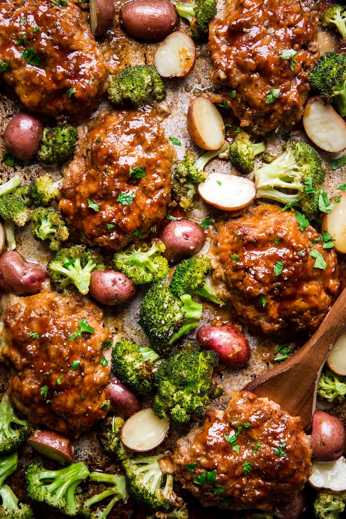 Italian-style meatloaf sheetpan with broccoli and potatoes shown with wooden spatula