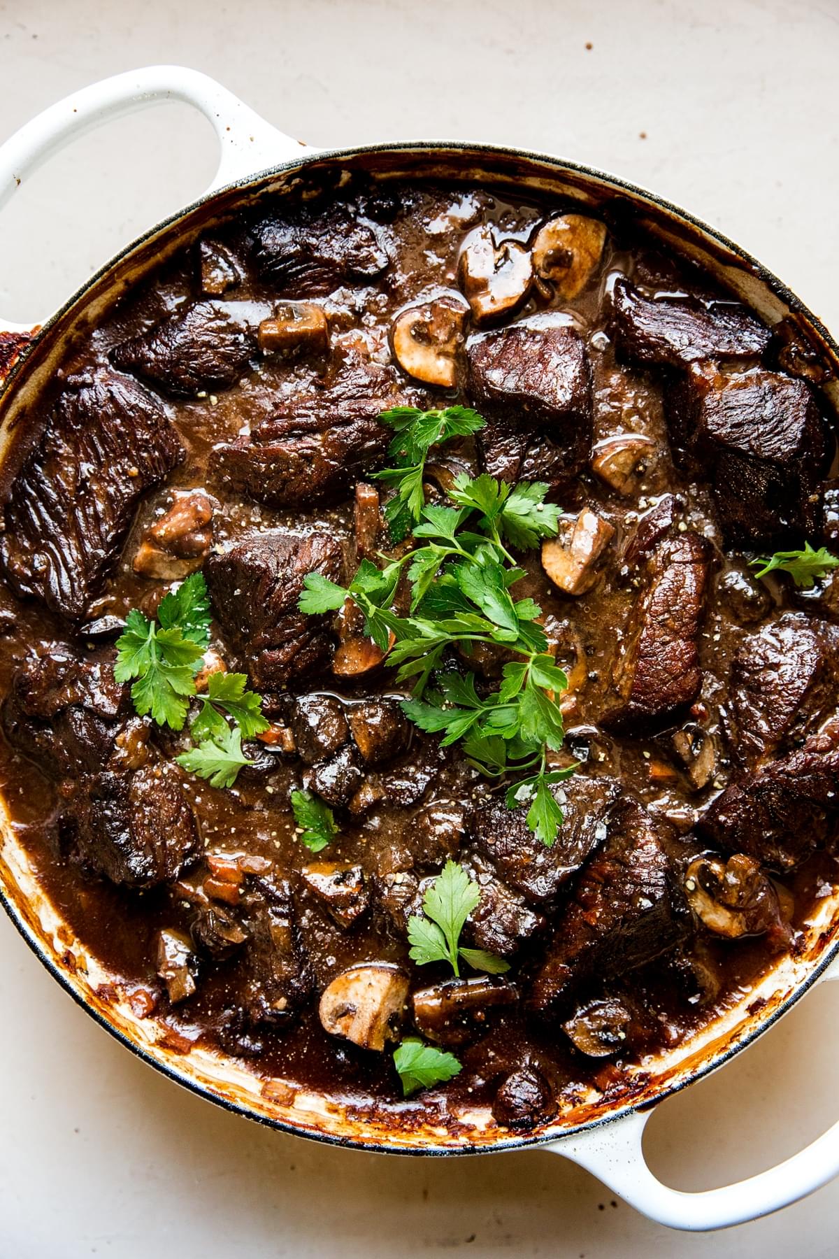 wine braised beef with mushrooms in a white braiser topped with parsley