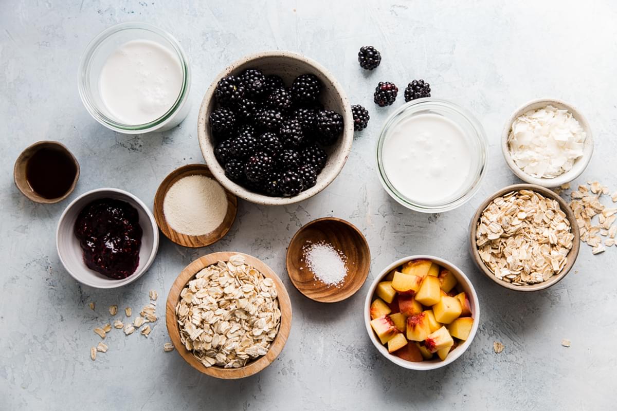 Ingredients for overnight oats shown in glass bowls including oats, berries, coconut milk and protein powder