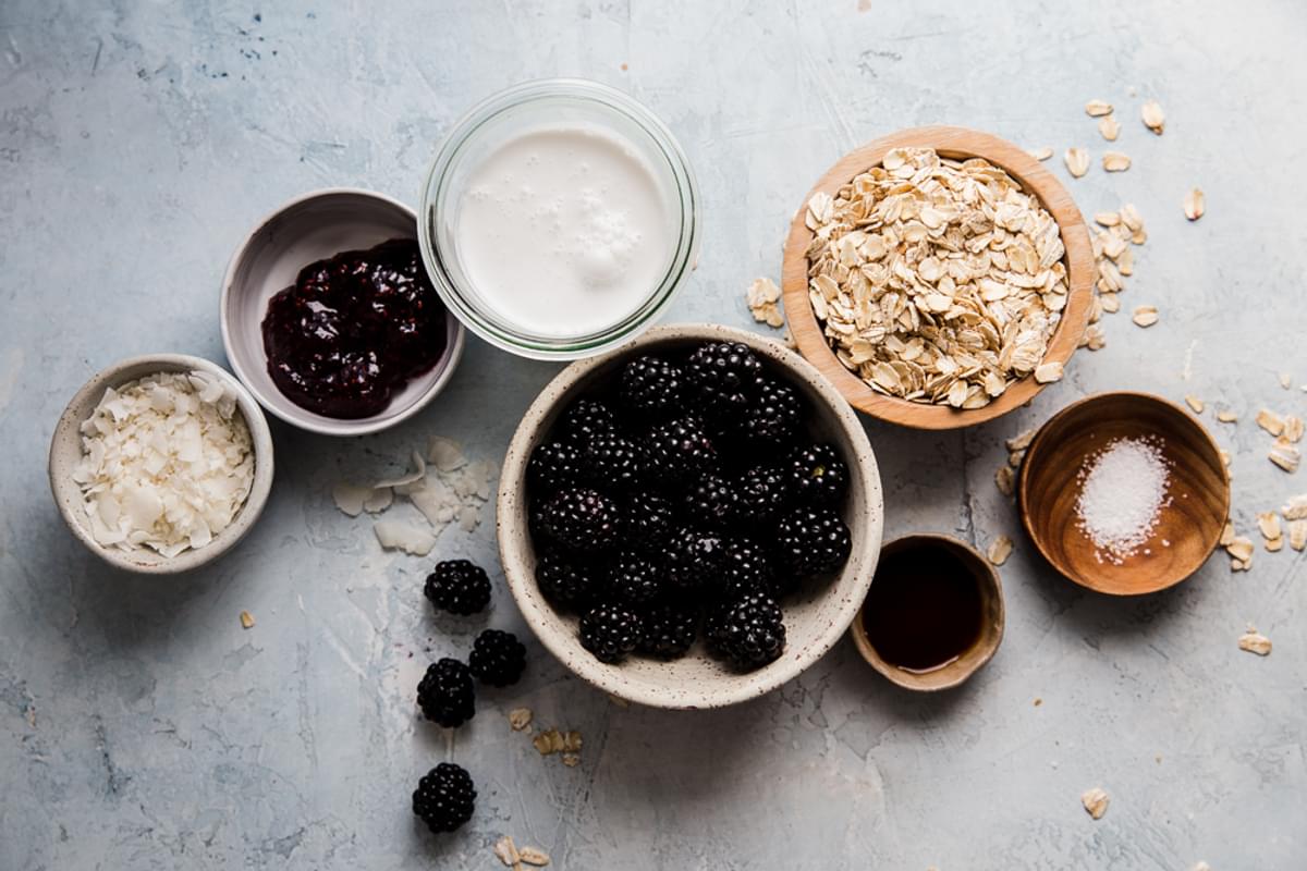 Ingredients for blackberry coconut overnight oats in glass bowls including oats, berries, coconut milk and vanilla