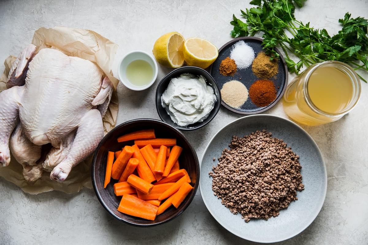 Ingredients for roast chicken with lentils show in  small bowls including a whole chicken, lentils, carrots and spices