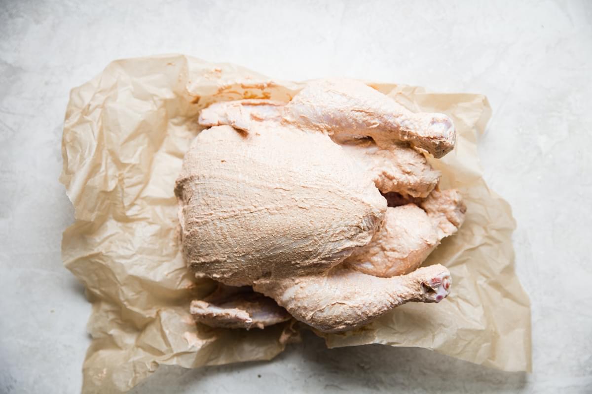 Whole chicken on parchment paper covered in yogurt marinade