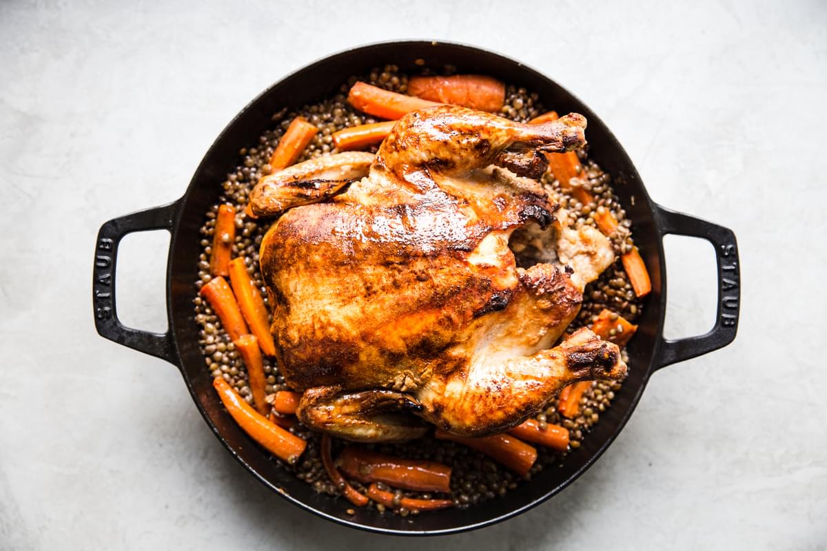 whole roast chicken over cooked lentils and carrots in a large skillet