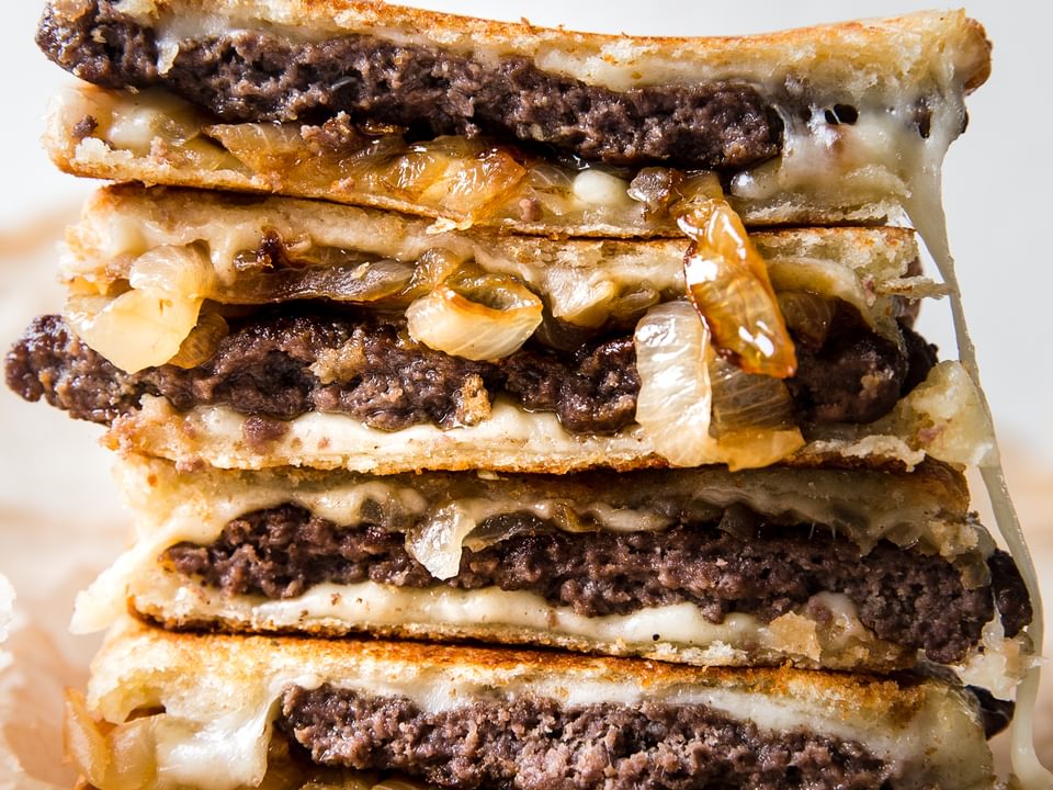 a patty melt stacked made with sourdough bread, caramelized onions, swiss cheese and mayo