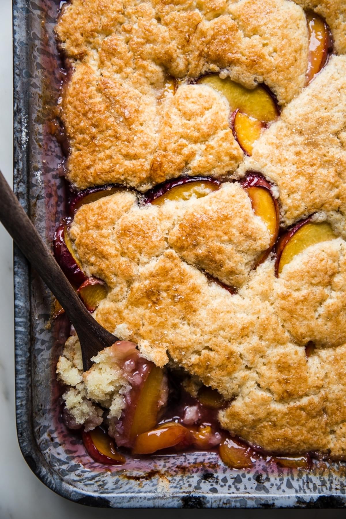 freshly baked peach cobbler in a baking dish with a spoon.