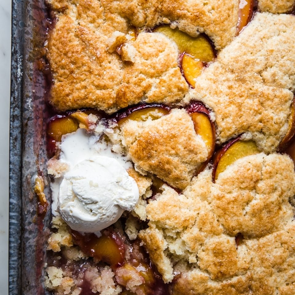 freshly baked peach cobbler in a baking tin with a scoop of ice cream