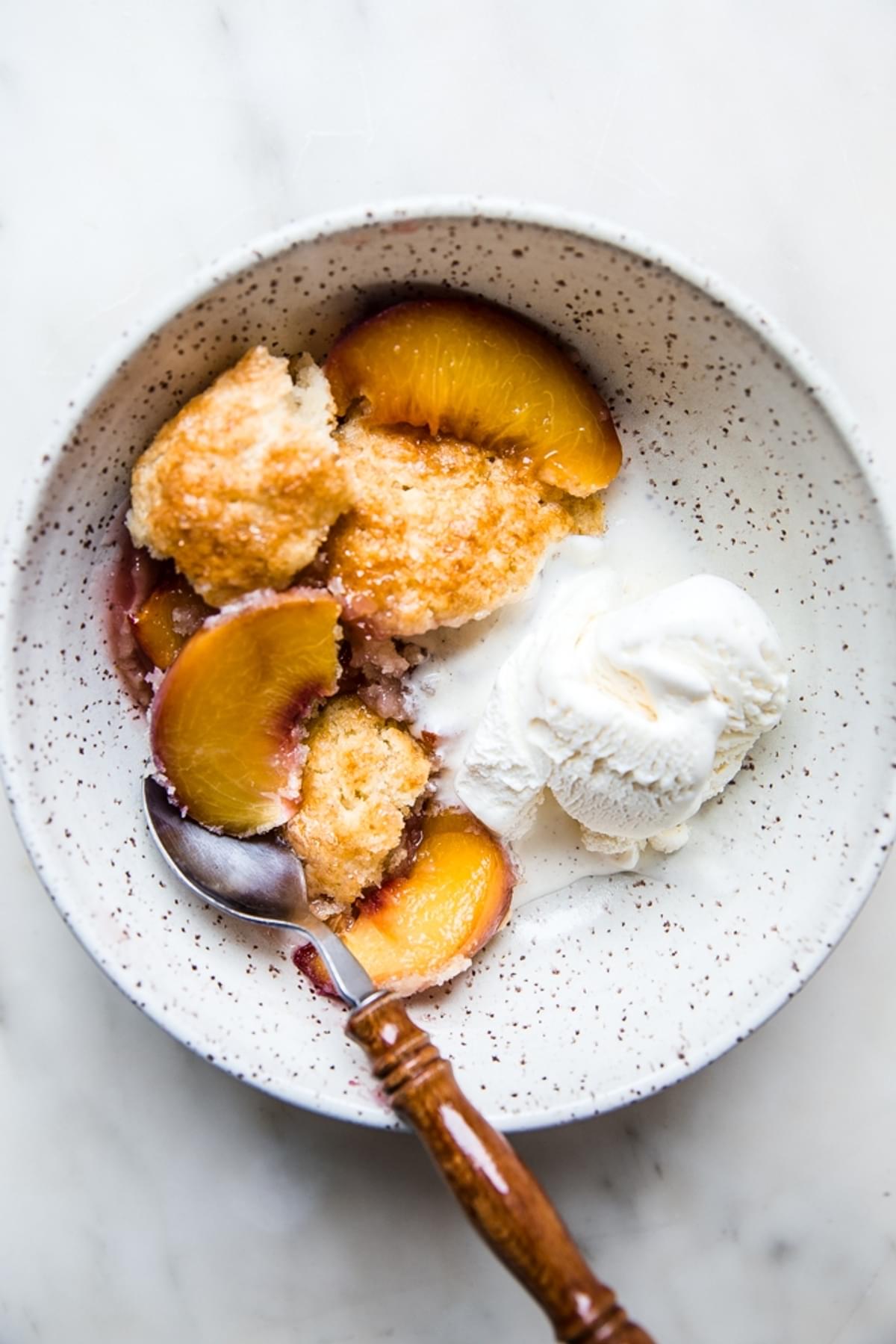 homemade peach cobbler in a bowl with a scoop of ice cream and a spoon.