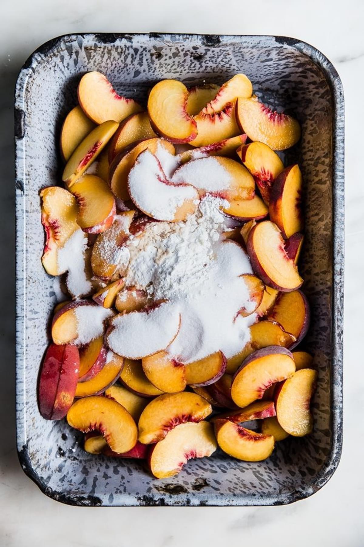 sliced yellow peaches in a baking tin with flour, sugar and butter