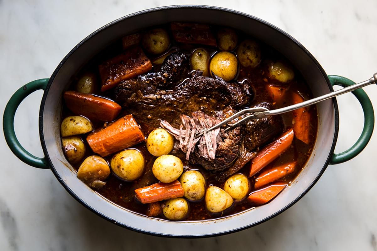 roasted pot roast with carrots and baby potatoes in an oval pot