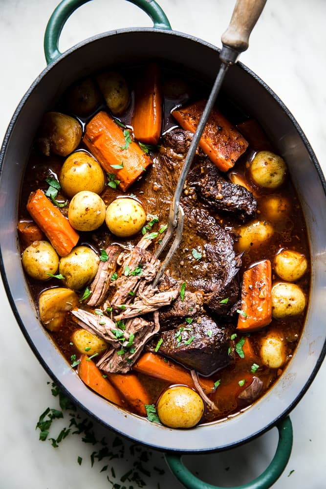 Pot roast in a large oval pot with wine broth, carrots and baby potatoes