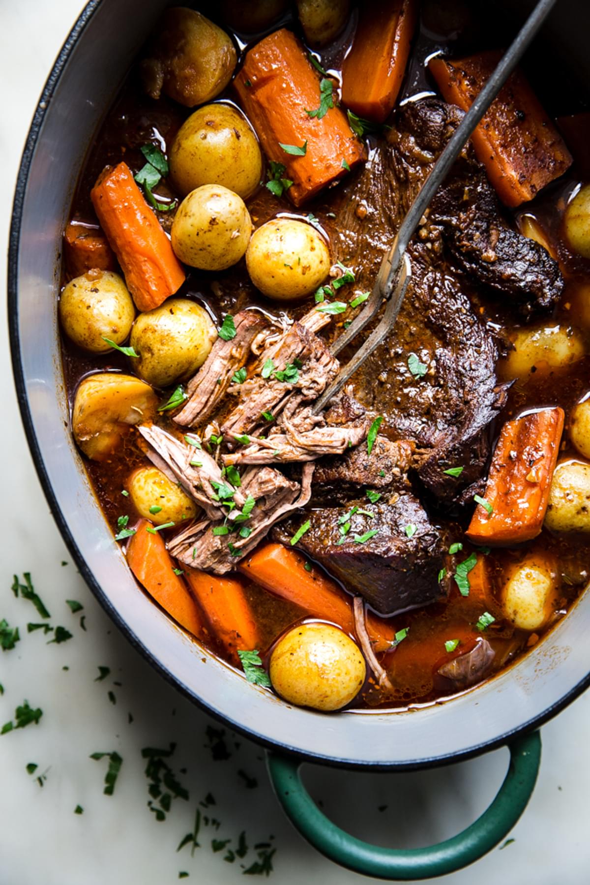 easy pot roast shown in a large pot with fork showing shredded beef along side potatoes and carrots