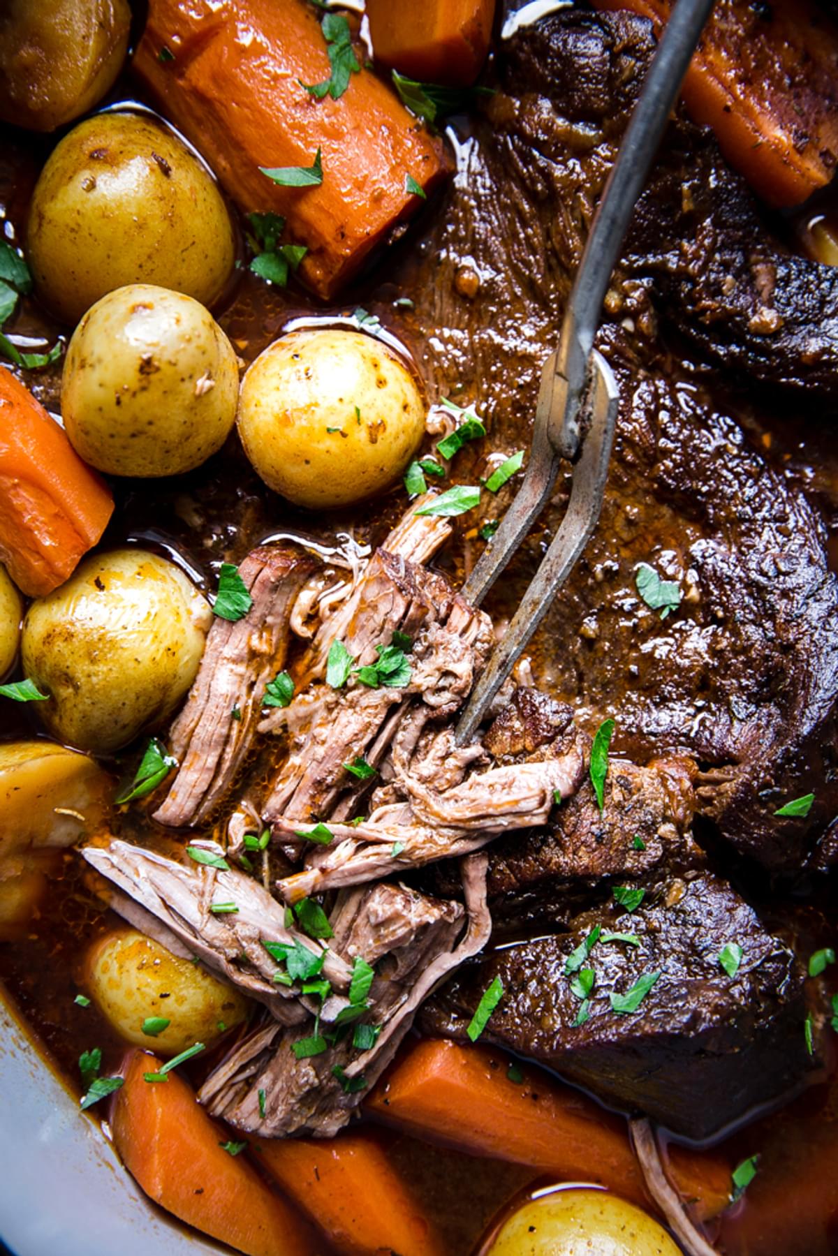 close up of a pot roast meat being served with a fork with carrots and potatoes