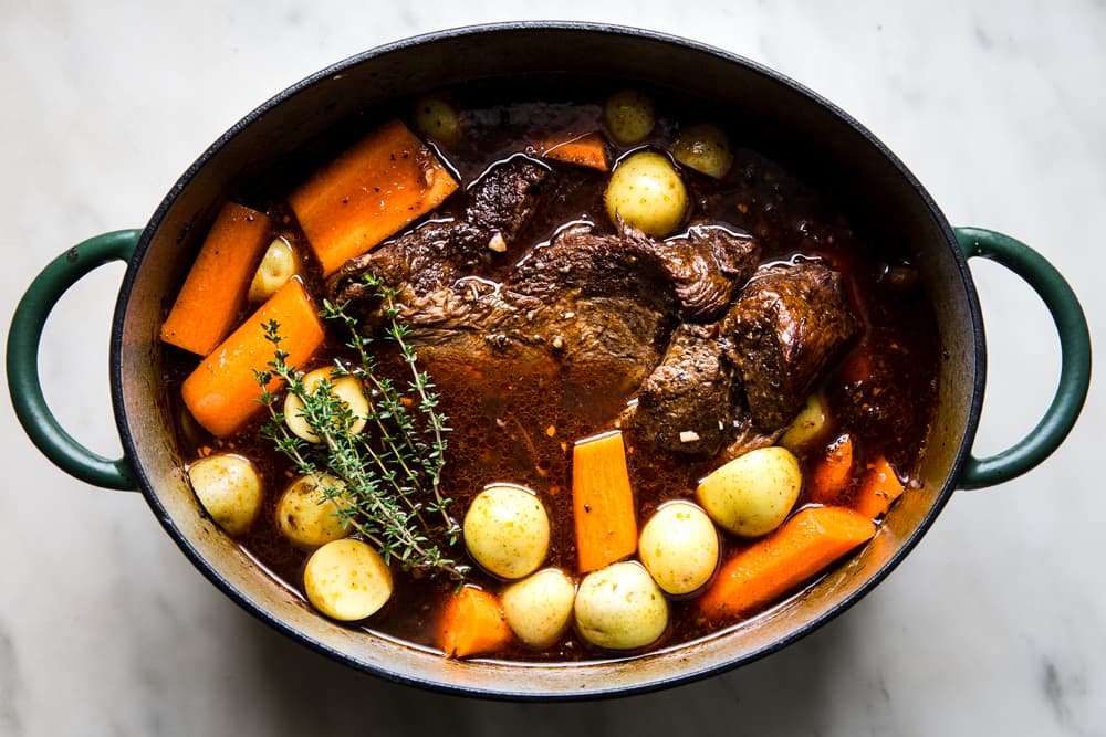Pot roast in red with shown with baby potatoes and carrots in a dutch oven