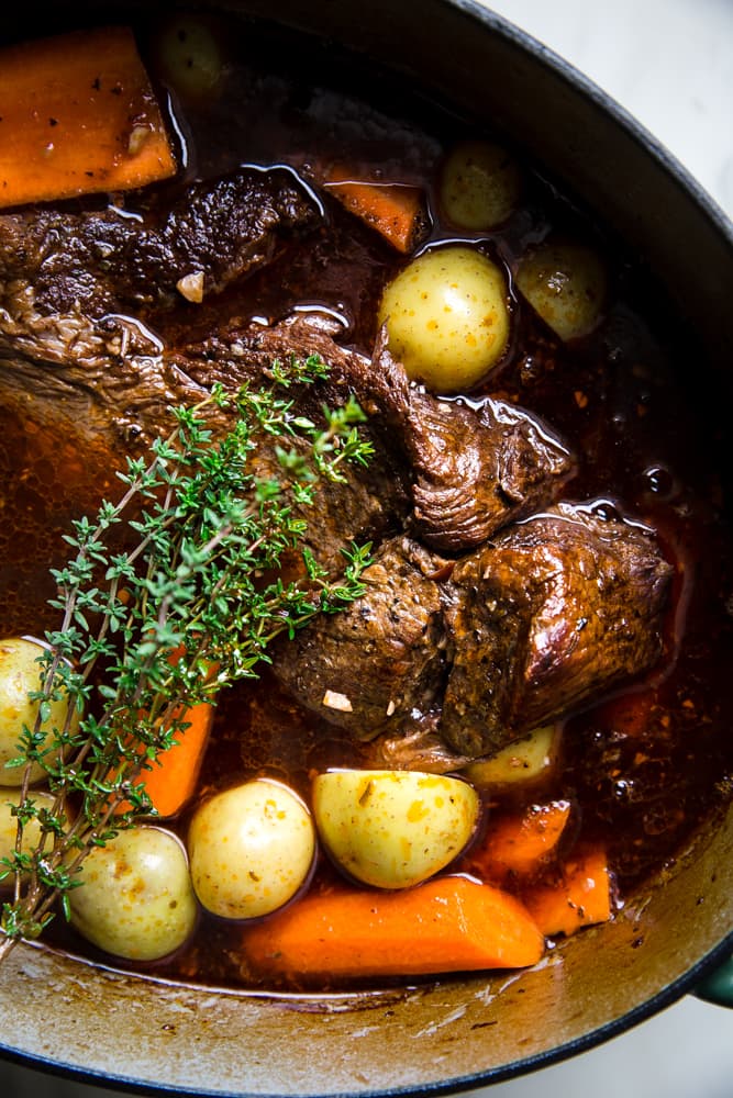 close up of pot roast shown in a dutch oven with with fresh herbs