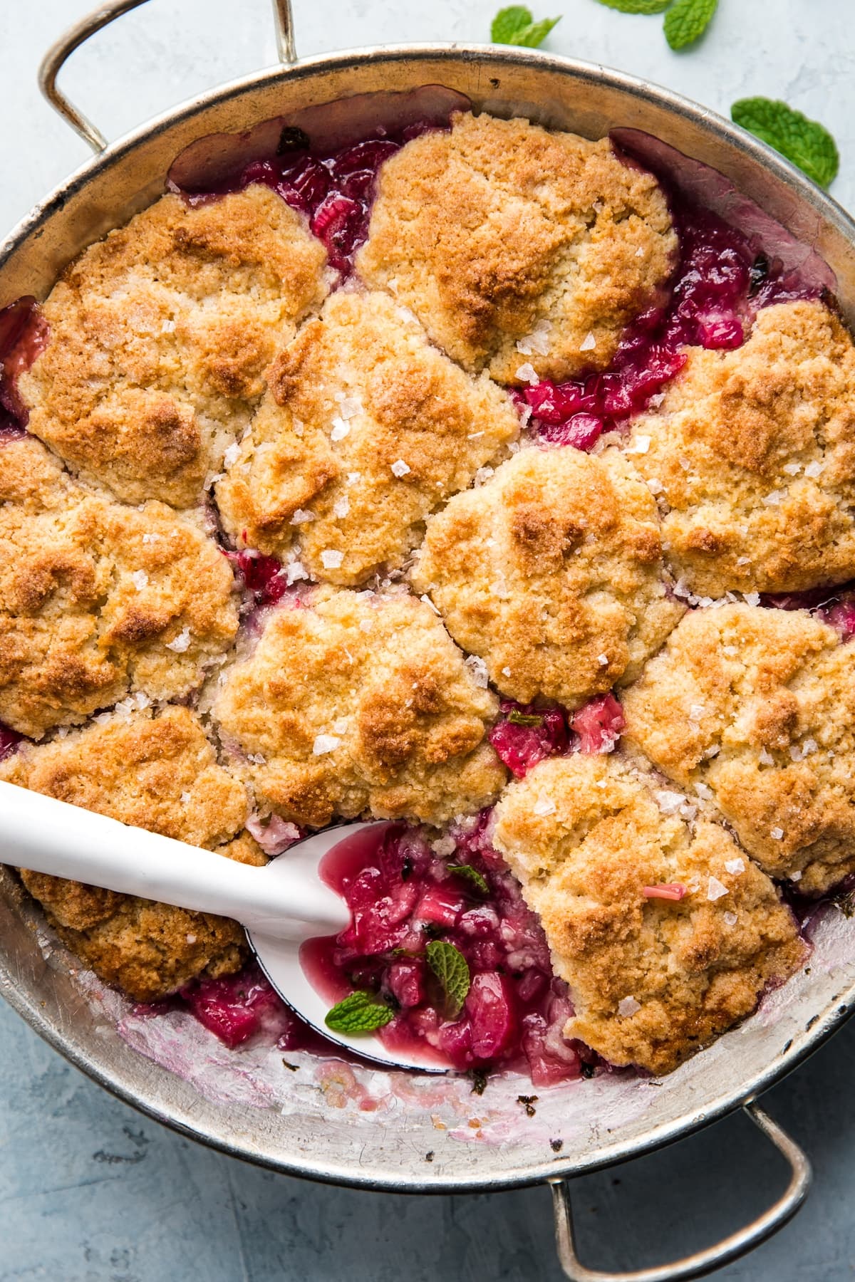 rhubarb cobbler with mint in a round baking dish with a large white metal spoon