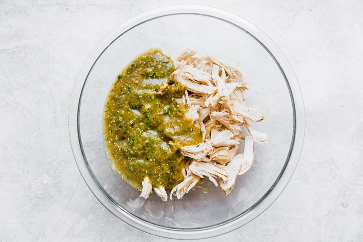 shredded chicken breasts shown in a glass bowl with salsa verde