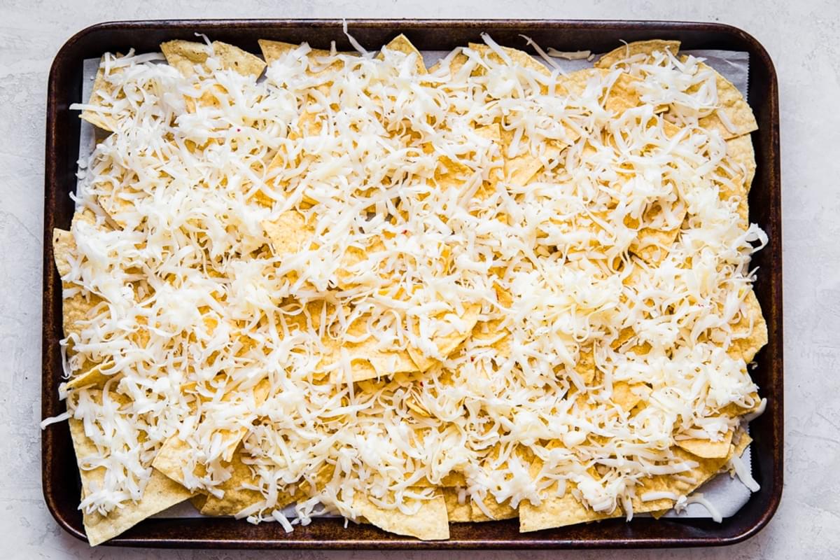 Shredded cheese on top of corn chips shown on a baking sheet
