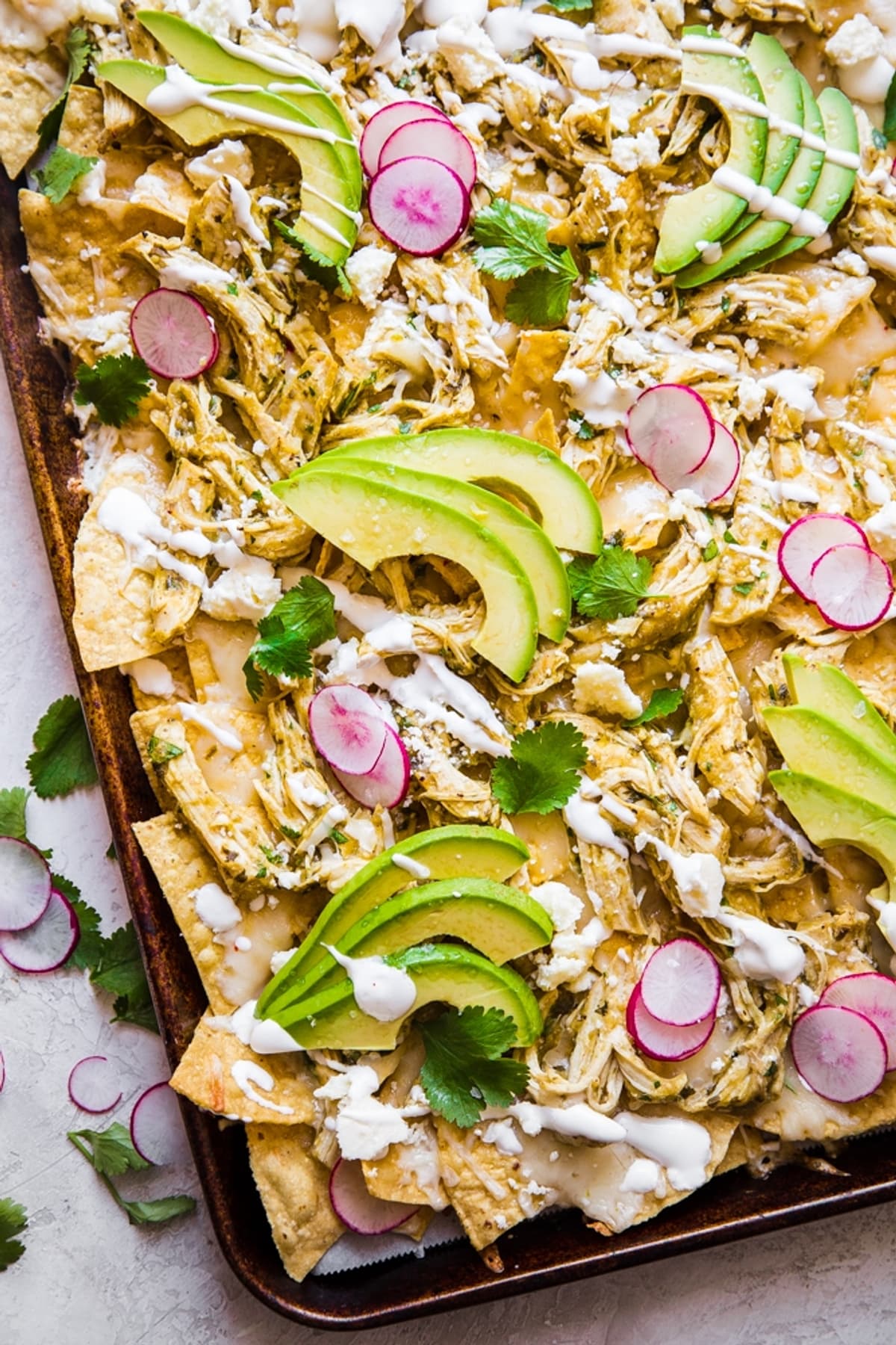 sheet pan of roasted salsa verde nachos topped with avocado and radishes