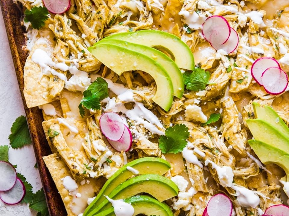 sheet pan of roasted salsa verde nachos topped with avocado and radishes