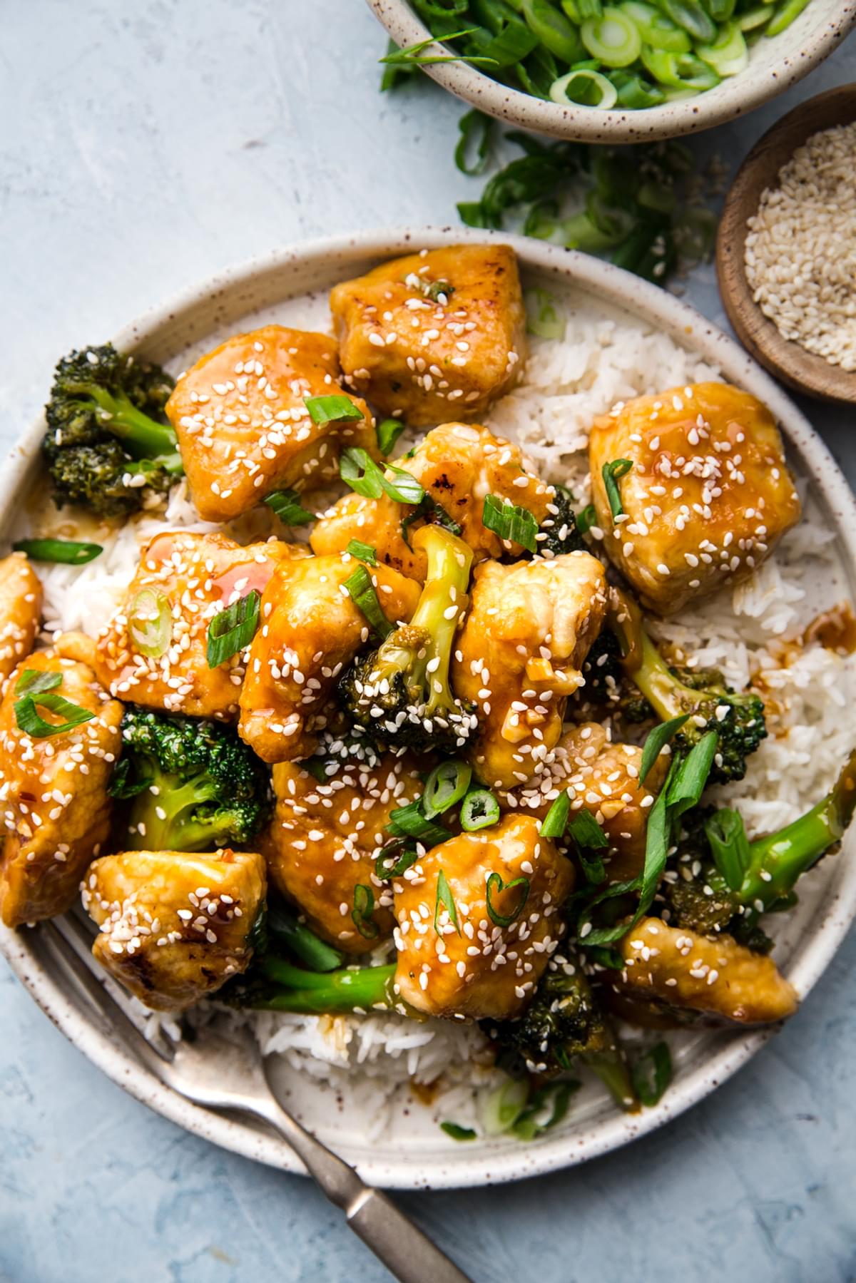 Sesame Chicken with Broccoli and rice on a plate with green onions and sesame seeds